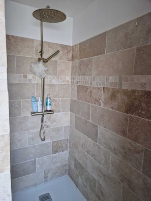 Une douche équipée d’un pommeau de douche à effet pluie, d’un pommeau de douche à main et d’une étagère pour les articles de toilette.