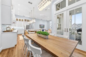 A modern kitchen with white cabinets, a wooden island, and a dining area with white chairs. - New 5 Bedroom Beach Home @Cinnamon Shore (Port Aransas)