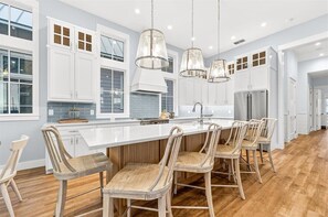 A modern kitchen with white cabinets, a large island, and bar stools. - New 5 Bedroom Beach Home @Cinnamon Shore (Port Aransas)