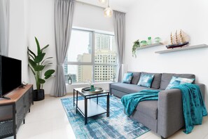 A modern living room with a grey sofa, a coffee table, a TV, and a large window with curtains. - bnbme - Bay Central - 1BR (Dubai)