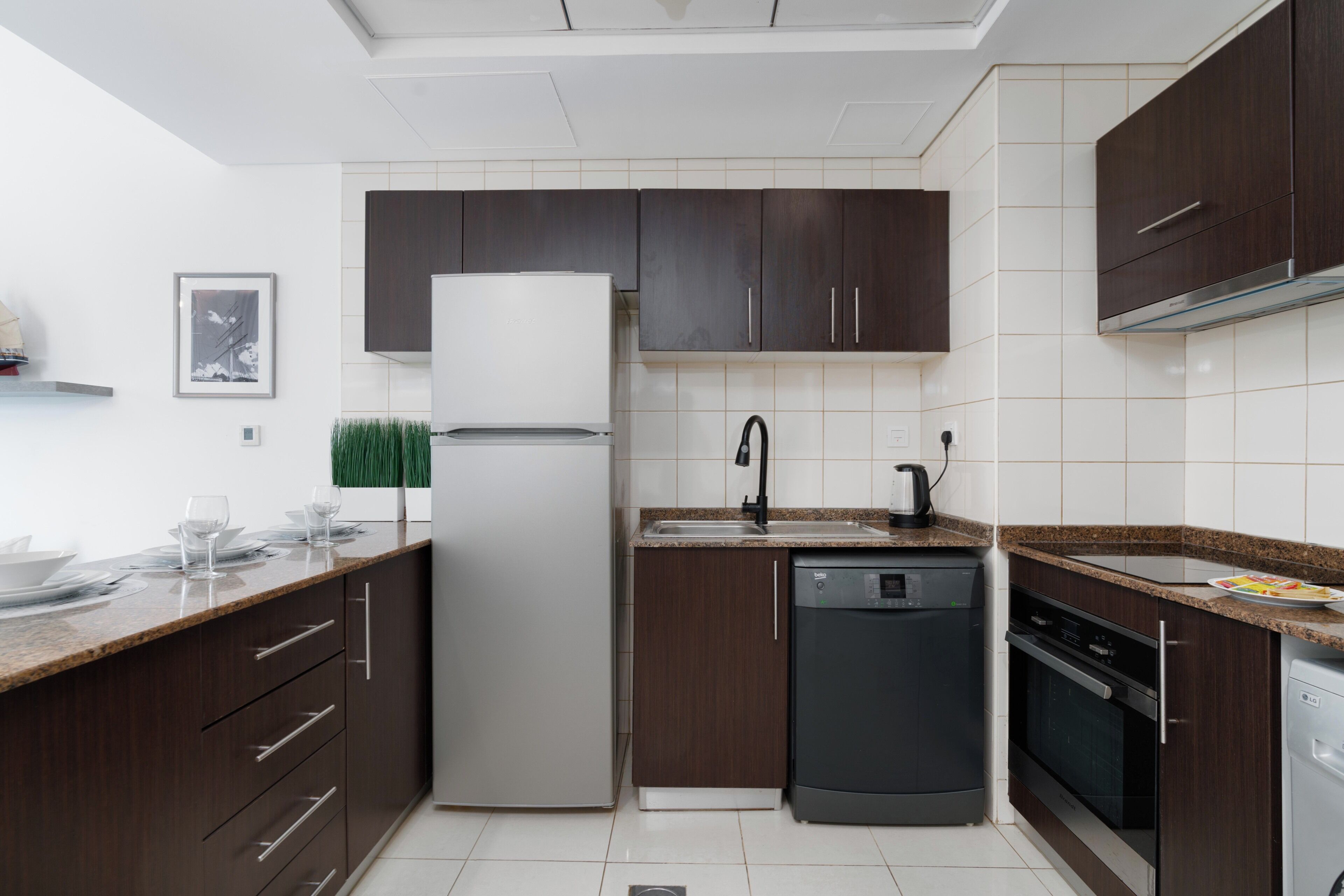 A modern kitchen with dark wooden cabinets, a white refrigerator, and a dishwasher.