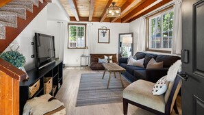 Un salon chaleureux avec un escalier en bois, une télévision, un canapé et une grande fenêtre.