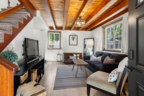 Ein gemütliches Wohnzimmer mit einer Holztreppe, einem Fernseher, einer Couch und einem großen Fenster.