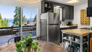 Une cuisine moderne dotée d’un réfrigérateur en acier inoxydable, d’une table à manger en bois et offrant une vue sur la mer.