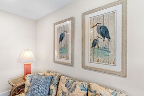 Ein Zimmer mit einer Couch, gerahmten Kunstwerken, einer Lampe und einem Korbstuhl.