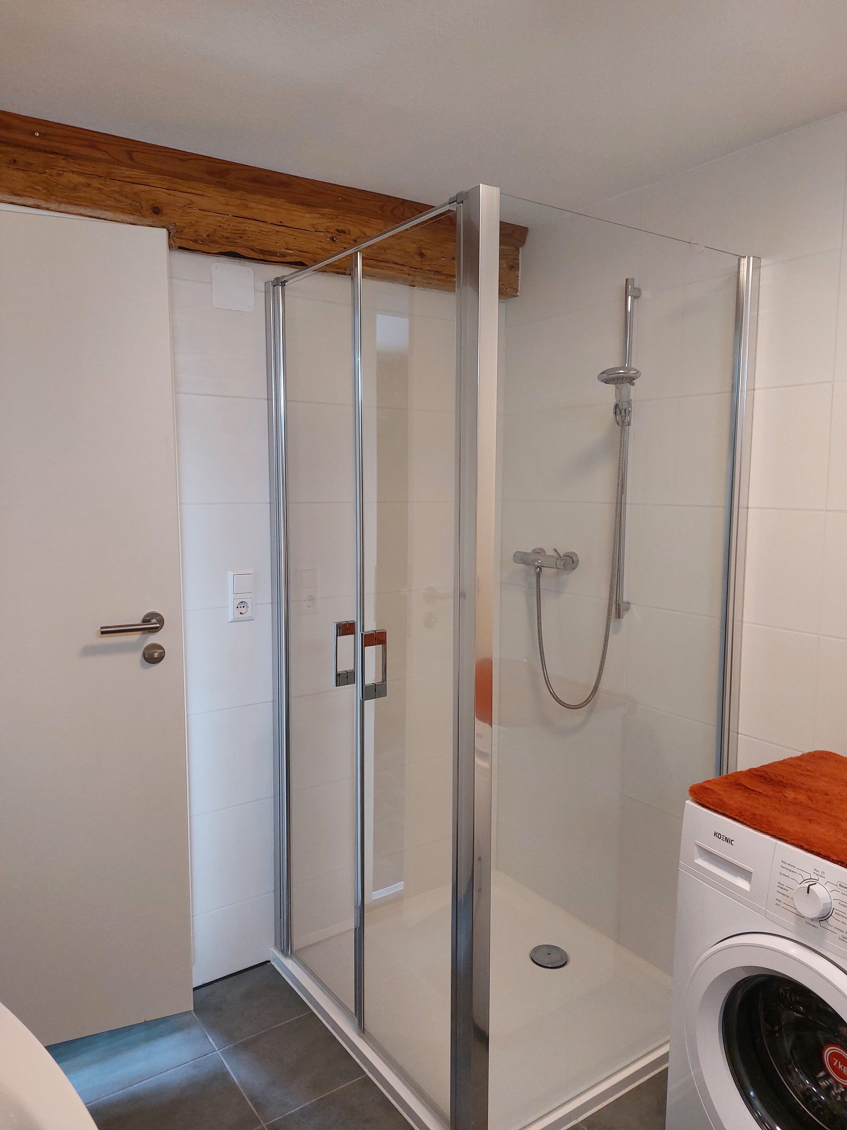 Een moderne badkamer met een douchecabine van glas, een witte wasmachine en een houten plafond.