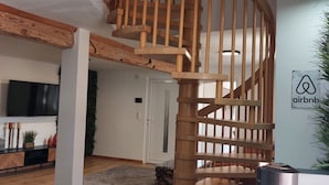 A modern interior with a wooden spiral staircase, a flat-screen TV, a plant, and a sign for Airbnb. - Maisonette with south-facing terrace & barbecue (Kapsweyer)