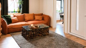 A living room with a sofa, a coffee table, a rug, and a wooden ceiling beam. - Maisonette with south-facing terrace & barbecue (Kapsweyer)