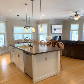 A modern kitchen with a central island, pendant lighting, and a dining area with wooden chairs. - Salt & Lime at Turner Tide (North Myrtle Beach)
