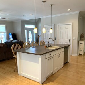 A modern kitchen with a central island, pendant lighting, and a view to the living area. - Salt & Lime at Turner Tide (North Myrtle Beach)