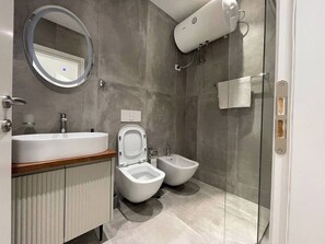 Ein modernes Badezimmer mit Waschbecken, Bidet, Toilette und Duschkabine aus Glas.