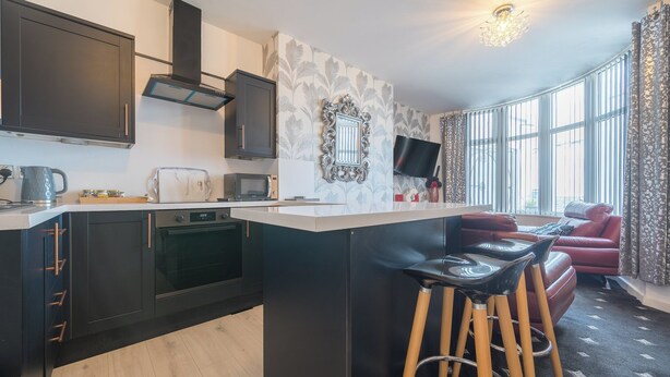 Een moderne keuken met donkere kastjes, een centraal eiland met krukken, een magnetron en een broodrooster.