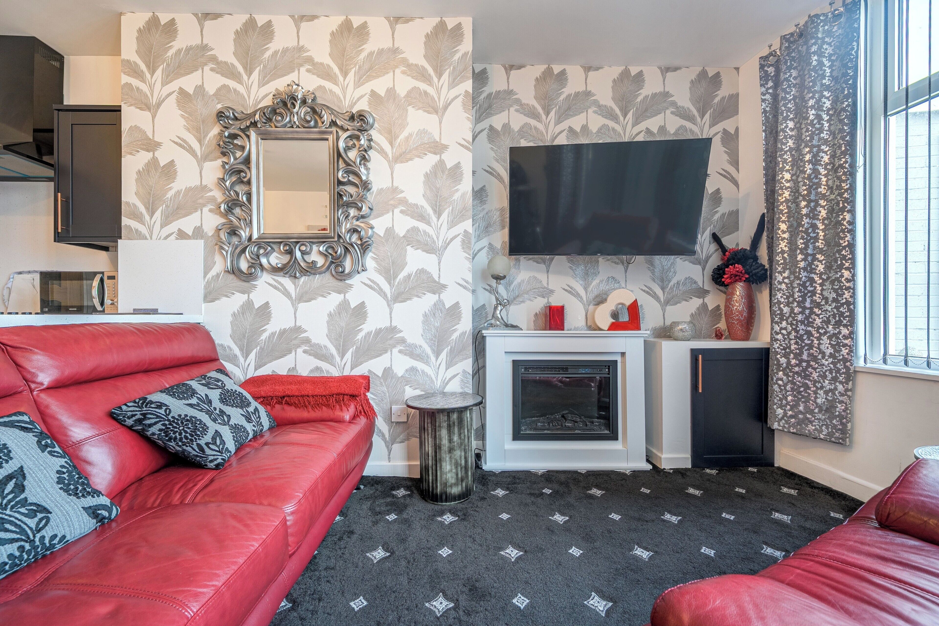 A living room with a red sofa, a fireplace, a TV, and patterned wallpaper.