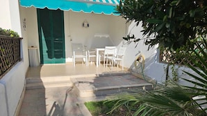 A patio with hexagonal tiles, white chairs, a green door, and a blue awning. - The villa is located 250 meters from the sandy beaches with crystal clear sea. (Baia Verde)