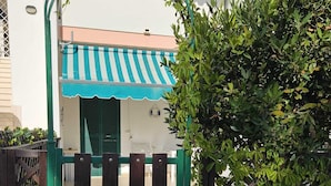 A gated entrance with a green gate, a white wall, and a building with a striped awning. - The villa is located 250 meters from the sandy beaches with crystal clear sea. (Baia Verde)