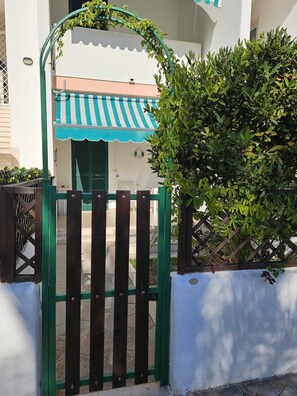 A gated entrance with a green gate, a white wall, and a building with a striped awning. - The villa is located 250 meters from the sandy beaches with crystal clear sea. (Baia Verde)