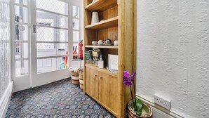 Hall d'albergo con tappeto a motivi, un armadietto in legno con oggetti decorativi, un estintore e un cartello che indica le camere disponibili.