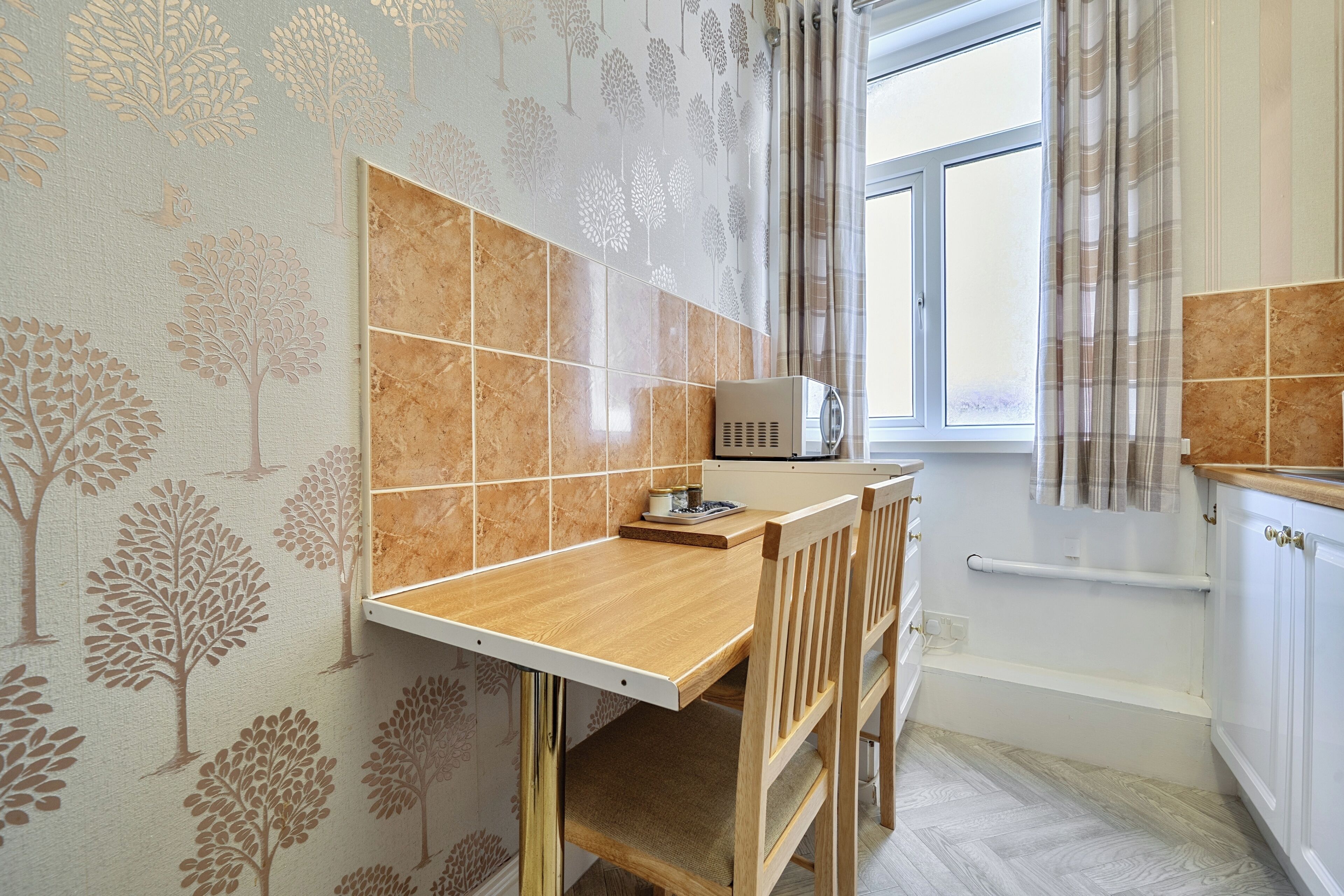 A kitchen with a wooden table, a microwave, and a window with curtains.