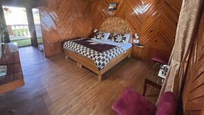 Una habitación con techo de madera en patrón de espiga, cama con ropa de cama estampada, una mesita de noche y una pequeña mesa con un vaso.