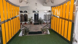 Un vestíbulo de hotel con una escalera central, un mostrador de recepción y vistas al acceso principal.