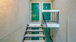 A staircase with green doors at the top, a white handrail, and a textured wall.