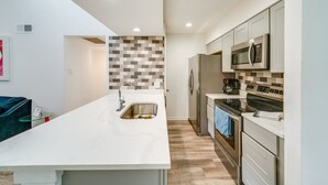 A modern kitchen with white cabinetry, a stainless steel refrigerator, a microwave, and an oven.
