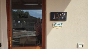 Eine Holztür mit einem Glasfenster, einem Willkommensschild und einem Schild mit der Zimmernummer D/3.