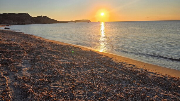 Ein Strand mit Sonnenuntergang, ruhiger See und steinigen Klippen.