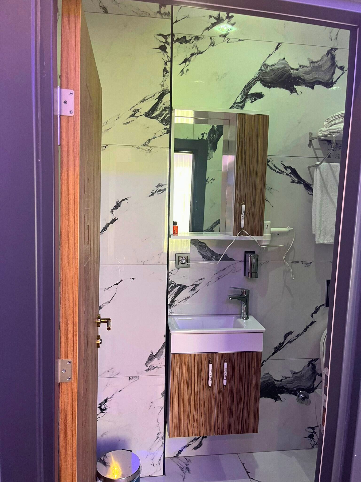 A modern bathroom with a glass partition, a wooden vanity, a mirror, a sink, and a toilet.