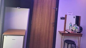 A room with a wooden door, a small desk with a chair, a refrigerator, and a ceiling light fixture. - Hisar Çeşme Hotel (Istanbul)