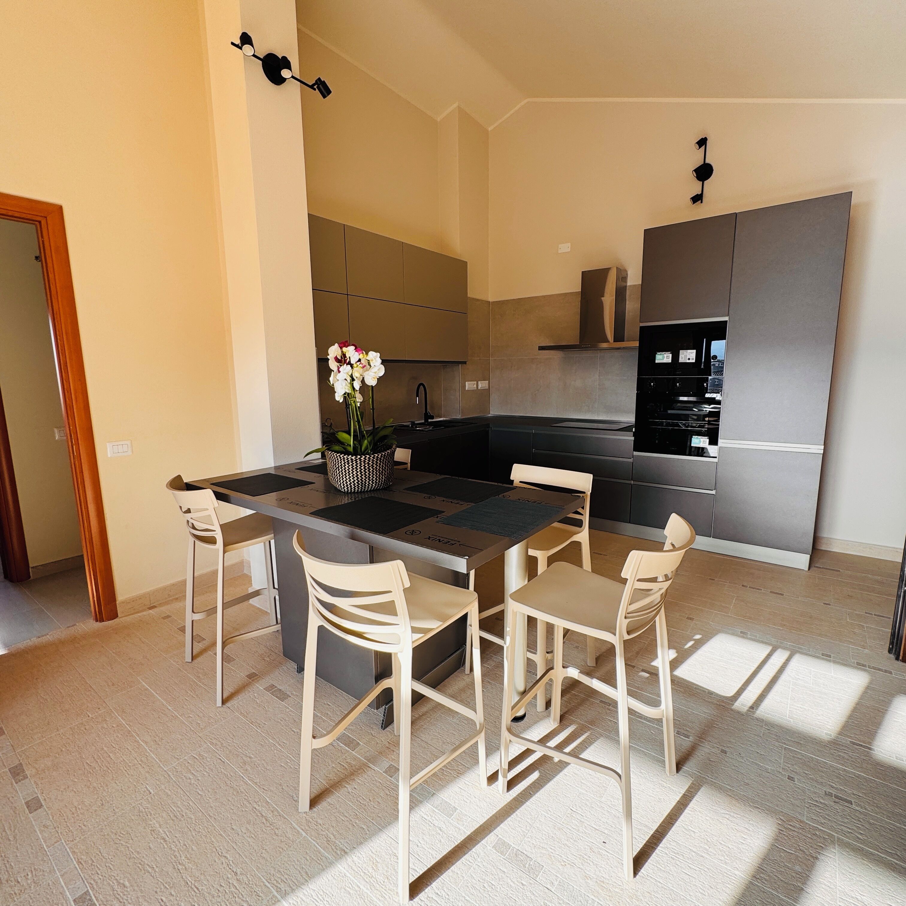 Une cuisine moderne avec un îlot central, quatre chaises et un vase de fleurs.