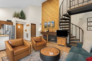 A modern living room with a fireplace, leather armchairs, a coffee table, and a staircase. - Cozy Mountain Condo - Pool, Sauna, & Hot Tub Access (Keystone)