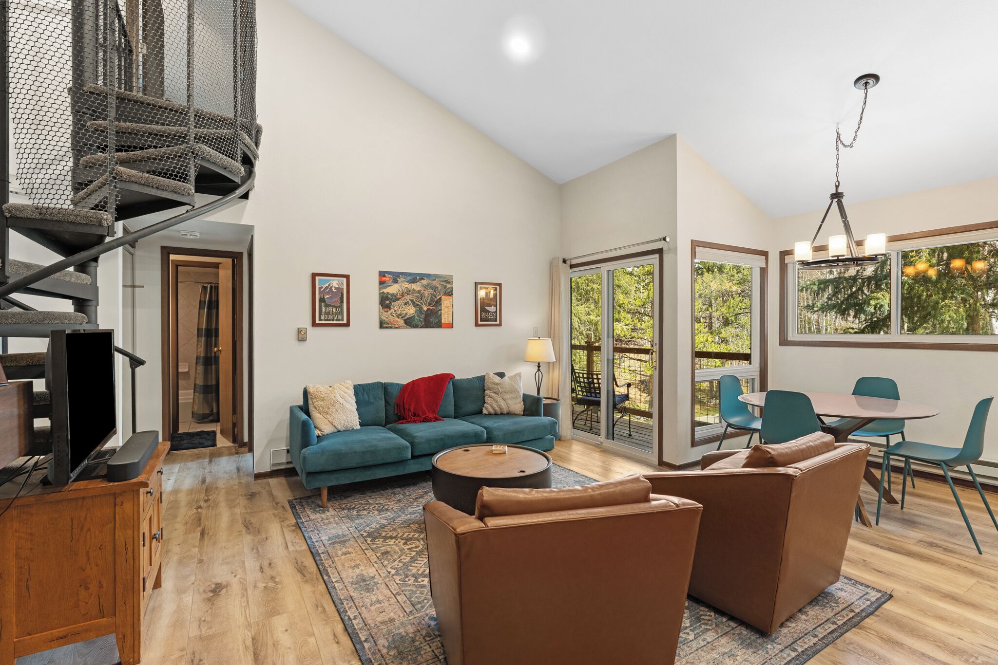 A modern living room with a blue sofa, brown armchairs, a coffee table, a TV, and a spiral staircase.