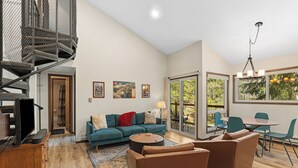 Een moderne woonkamer met een blauwe bank, bruine fauteuils, een salontafel, een televisie en een spiltrap.