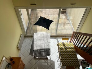 A room with a large window, a metal table, a wooden chair, and a patterned tablecloth. - Duplex near the beach - 6 guests (Arzon)