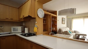 Cocina compacta con armarios de madera, microondas, estufa y un reloj en la pared.
