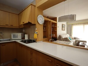 A compact kitchen with wooden cabinets, a microwave, a stove, and a clock on the wall. - Apartment with AC and pool - 4 guests (Lloret de Mar)