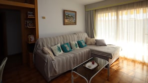 Una sala de estar con un sofá, una mesa de centro, una estantería y un cuadro en la pared.