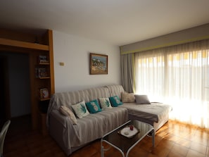 A living room with a sofa, a coffee table, a bookshelf, and a painting on the wall. - Apartment with AC and pool - 4 guests (Lloret de Mar)