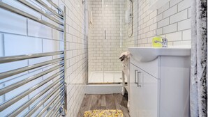 A modern bathroom with white tiled walls, a glass shower enclosure, a white sink with a yellow soap dispenser, and a wooden floor. - First Floor 2-bed Apartment With Sea View (Blackpool)