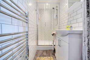 Ein modernes Badezimmer mit weißen Fliesen, einer Glasdusche, einem weißen Waschbecken mit gelbem Seifenspender und Holzboden.