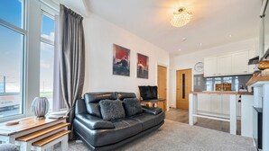 A modern living room with a leather sofa, a wooden coffee table, and a view through large windows. - First Floor 2-bed Apartment With Sea View (Blackpool)