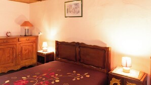 Un dormitorio con cabecera de madera, cama con colcha floral, cómoda de madera, dos lámparas de noche y un cuadro en la pared.