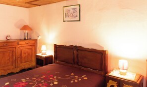 Une chambre à coucher avec une tête de lit en bois, un lit recouvert d’une couvre-lit à motifs floraux, une commode en bois, deux lampes de chevet et un tableau encadré accroché au mur.