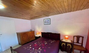 A bedroom with a wooden ceiling, a bed with a floral bedspread, a wooden nightstand with a lamp, a wooden dresser, and a framed picture on the wall.