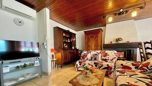 Una sala de estar con televisor, sofá, chimenea, aparador de madera y un reloj en la pared.