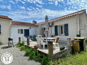 Une cour avec une table et des chaises, un barbecue et un parasol.