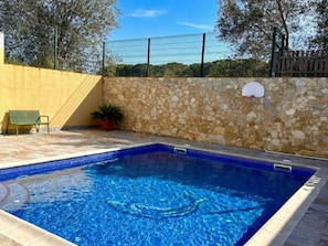 Ein Schwimmbecken mit Steinmauern, einem Basketballkorb und einer Bank.