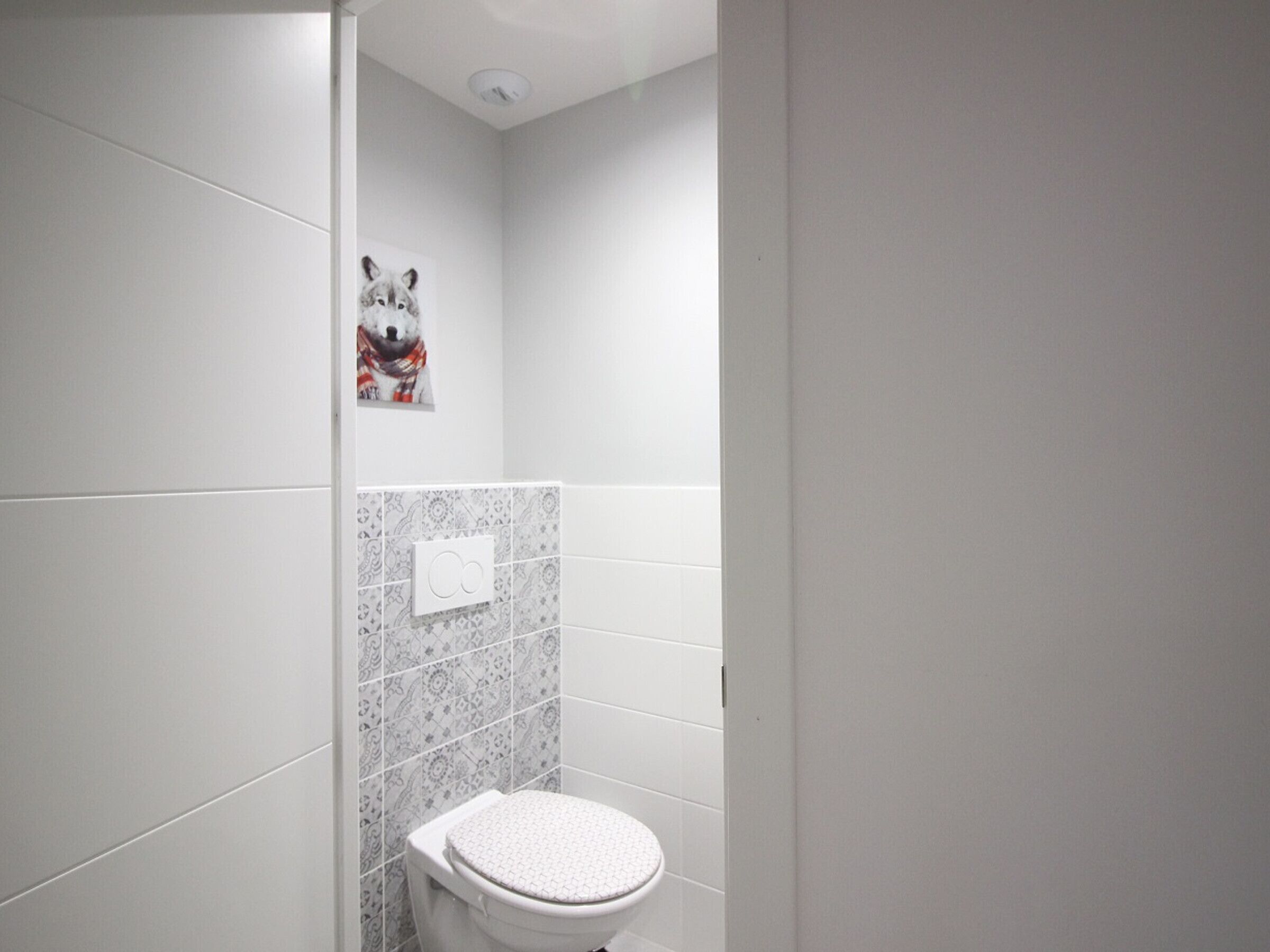 A small bathroom with a toilet, a wall-mounted light switch, and a decorative animal poster.