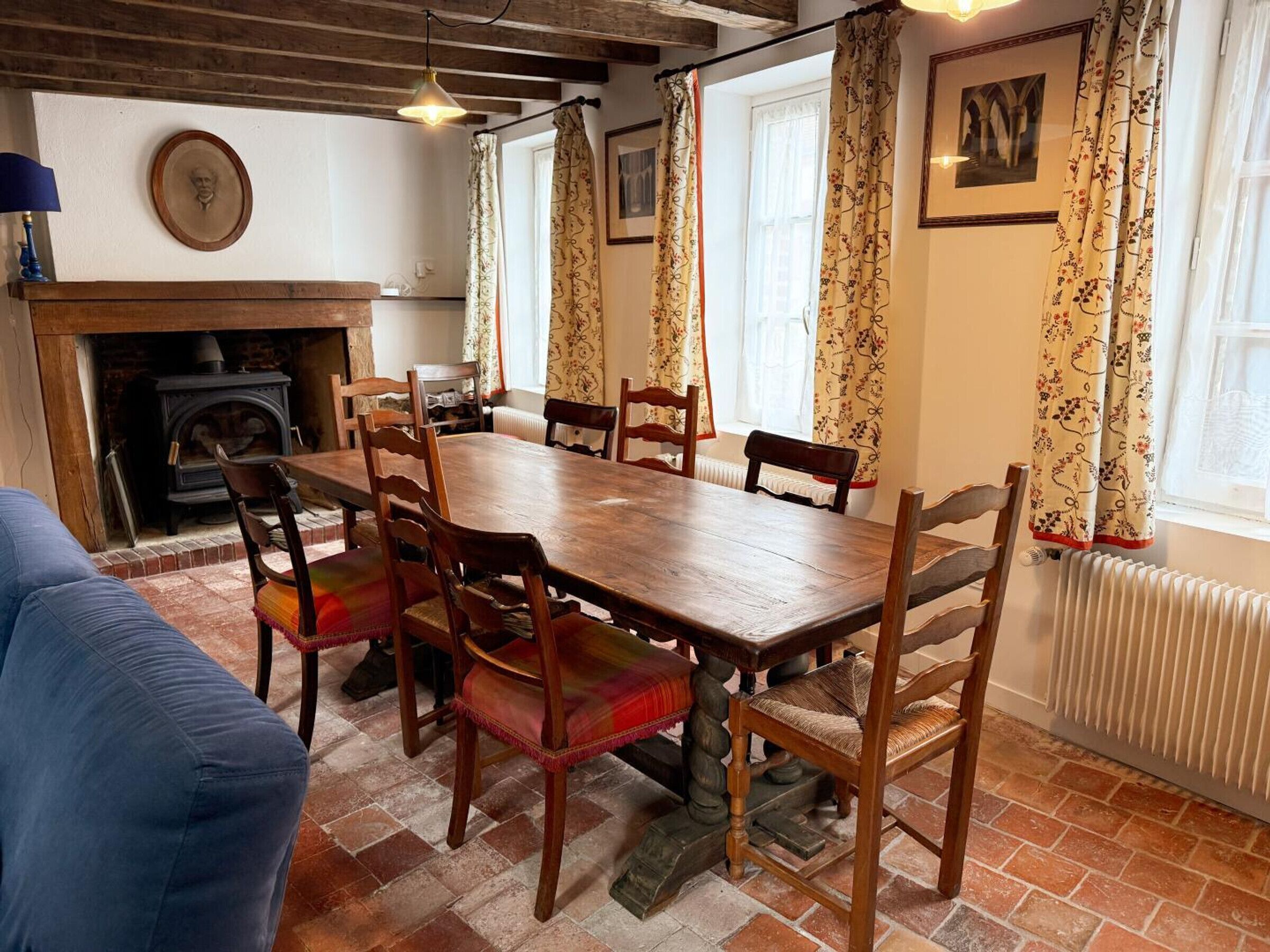 Ein Esszimmer mit Holztisch, Stühlen, einem Kamin und gemusterten Vorhängen.